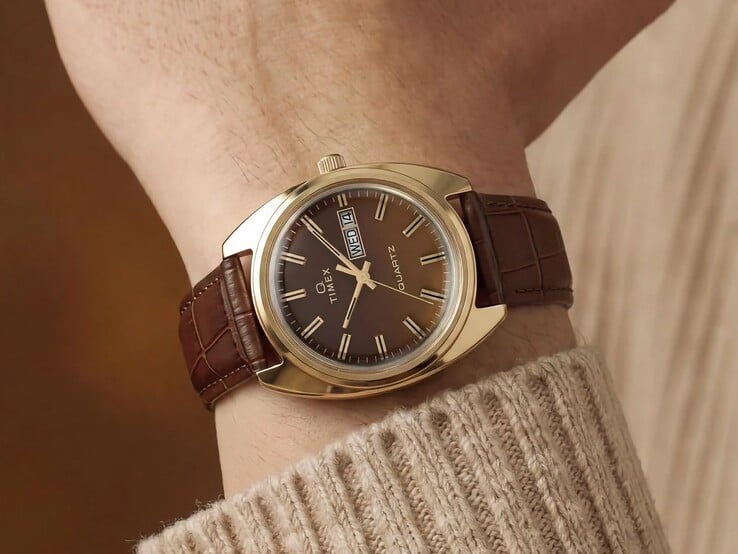 Timex Q 1976 Day and Date com mostrador fumé castanho e caixa em tom dourado, mostrado num pulso com uma bracelete de couro castanho.