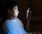 Adolescente em um quarto escuro olhando para um smartphone iluminado