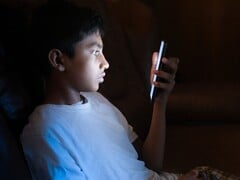 Adolescente em um quarto escuro olhando para um smartphone iluminado
