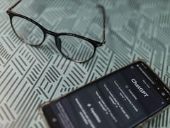 Smartphone com o aplicativo ChatGPT aberto ao lado de um par de óculos sobre uma superfície estampada