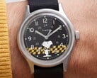 Close-up do mostrador preto do Timex MK1, exibindo o Snoopy contra um padrão xadrez amarelo e preto, com marcadores de horas em algarismos arábicos e ponteiros luminosos.