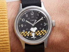 Close-up do mostrador preto do Timex MK1, exibindo o Snoopy contra um padrão xadrez amarelo e preto, com marcadores de horas em algarismos arábicos e ponteiros luminosos.