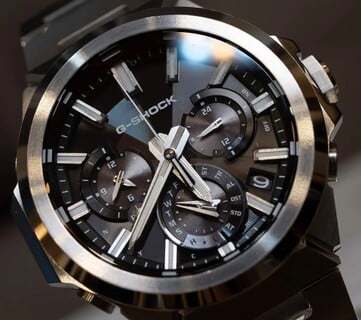 Close-up do Casio G-Shock GST-W1000D-1A com mostrador preto, mostrando seus três submostradores, marcadores de horas luminosos, ponteiros facetados e luneta de aço inoxidável com acabamento múltiplo.