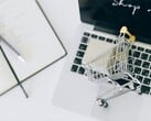 Carrinho de compras em miniatura no teclado de um laptop, com a mensagem “Compre agora” na tela