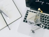 Carrinho de compras em miniatura no teclado de um laptop, com a mensagem “Compre agora” na tela