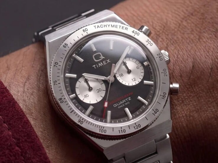 O relógio Timex Q Timex Continental Chronograph TW2Y93200 no pulso, com mostrador preto radial no estilo CD, dois submostradores prateados, luneta taquimétrica, marcadores luminosos e uma pulseira integrada de aço inoxidável.