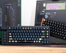 Teclados de efeito Hall Lemokey L1 HE Keychron K4 HE em uma mesa, em frente a uma caixa e um laptop