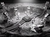 Relógio digital Casio x GRAGG LW-204GRAGG-1BDF exposto em um suporte escultural prateado, rodeado por astronautas em miniatura e objetos inspirados em metal fundido.