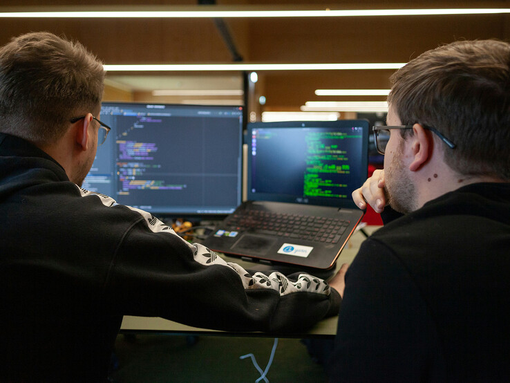 Pesquisadores analisando código em monitores duplos (Fonte da imagem: Flipsnack / Unsplash)
