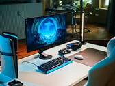 Uma configuração de gaming minimalista em estúdio, com o monitor Sony Inzone M10S II sobre uma mesa branca, ao lado de um console PlayStation 5 Pro na vertical, teclado mecânico, mouse sem fio e fone de ouvido com uma discreta iluminação azul.