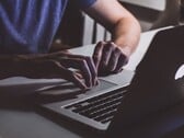 Mãos digitando no teclado de um MacBook sob luz fraca, com o logotipo da Apple brilhando
