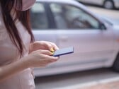 Uma mulher digitando em seu smartphone com um carro prateado ao fundo