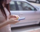 Uma mulher digitando em seu smartphone com um carro prateado ao fundo