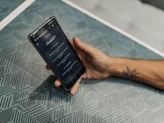 Mão segurando um smartphone com o aplicativo ChatGPT aberto sobre uma mesa estampada