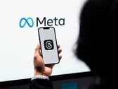 Uma mão segura um smartphone em frente a um grande logotipo da Meta
