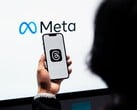 Uma mão segura um smartphone em frente a um grande logotipo da Meta