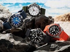 Quatro relógios de mergulho Citizen Promaster Marine nas cores branca, preta, azul e laranja, expostos sobre rochas à beira-mar.