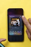 Um smartphone OnePlus exibindo o widget do reprodutor de mídia, com um usuário tocando no ícone de saída de áudio para acessar os controles de compartilhamento de áudio via Bluetooth.