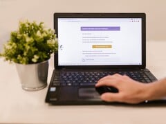Um laptop sobre uma mesa, exibindo uma caixa de entrada de e-mail aberta, com um vaso de planta ao lado.