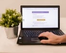 Um laptop sobre uma mesa, exibindo uma caixa de entrada de e-mail aberta, com um vaso de planta ao lado.