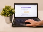 Um laptop sobre uma mesa, exibindo uma caixa de entrada de e-mail aberta, com um vaso de planta ao lado.
