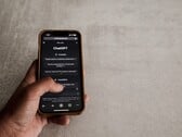 Mão segurando um smartphone que exibe a interface do ChatGPT sobre uma superfície de pedra cinza