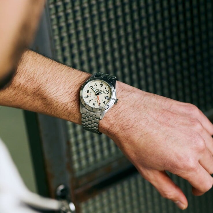 Vista frontal do Seiko 5 Sports Field GMT HDB002 com mostrador creme, ponteiro GMT laranja, luneta fixa de 24 horas e pulseira de aço inoxidável.