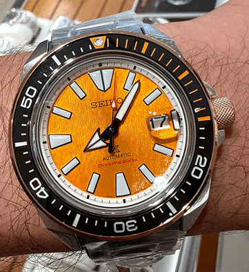 Close-up do Seiko Prospex HBB005K1, mostrando seu mostrador âmbar texturizado, marcadores de horas luminosos de grandes dimensões, ponteiros largos, janela de data e luneta de mergulho preta com marcações em laranja.