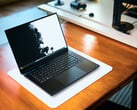Um notebook para jogos Razer Blade 16, na cor preto fosco, aberto, apoiado sobre um tapete de mesa branco sobre uma mesa de madeira em tom quente, exibindo um papel de parede vívido em preto e branco.