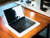 Um notebook para jogos Razer Blade 16, na cor preto fosco, aberto, apoiado sobre um tapete de mesa branco sobre uma mesa de madeira em tom quente, exibindo um papel de parede vívido em preto e branco.
