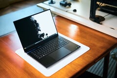Um notebook para jogos Razer Blade 16, na cor preto fosco, aberto, apoiado sobre um tapete de mesa branco sobre uma mesa de madeira em tom quente, exibindo um papel de parede vívido em preto e branco.
