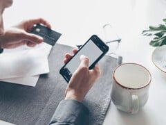 Pessoa digitando em um smartphone enquanto segura um cartão bancário na outra mão