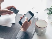 Pessoa digitando em um smartphone enquanto segura um cartão bancário na outra mão