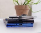 Pilha de smartphones dobráveis representando o conceito do futuro Apple iPhone Fold, colocados em uma mesa branca com um vaso de plantas ao fundo (Fonte da imagem: Notebookcheck)