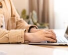 Mãos digitando no teclado de um laptop aberto sobre uma mesa bem iluminada