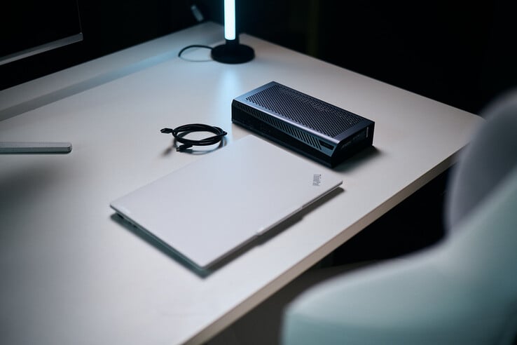 Um laptop ThinkPad branco fechado, ao lado da eGPU compacta Aorus RTX 5060 Ti AI Box e de um cabo Thunderbolt em espiral sobre uma mesa.