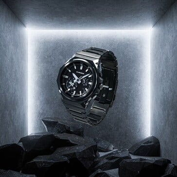 G-Shock GST-B1000BD-1A suspenso acima de pedras escuras em um espaço de exibição de concreto, destacando sua construção em aço inoxidável preto.