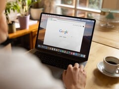 Pessoa usando um laptop com a página inicial do Google aberta, ao lado de uma xícara de café