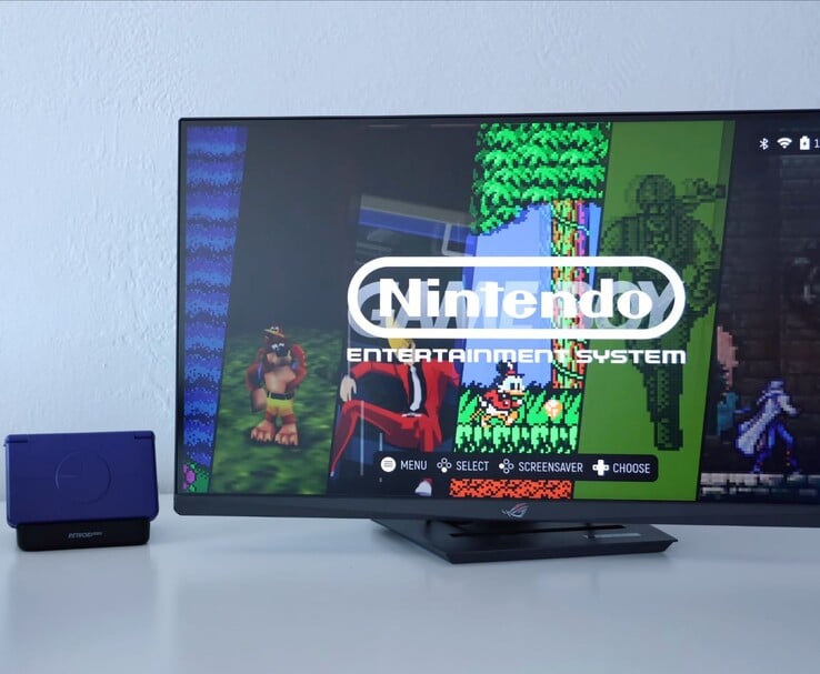 Retroid Pocket Flip 2 em roxo colocado em um dock ao lado de um monitor, com a tela da TV mostrando uma interface de emulador de NES retrô. (Fonte da imagem: Retro Game Corps no YouTube)