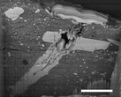 Imagem de microscópio eletrônico de varredura de uma cratera de impacto de micrometeorito em uma partícula de material do asteroide Bennu (Fonte da imagem: NASA, e Zia Rahman)