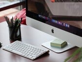 Um iMac sobre uma mesa, com a dock do macOS visível na tela e um teclado da Apple à sua frente