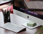 Um iMac sobre uma mesa, com a dock do macOS visível na tela e um teclado da Apple à sua frente