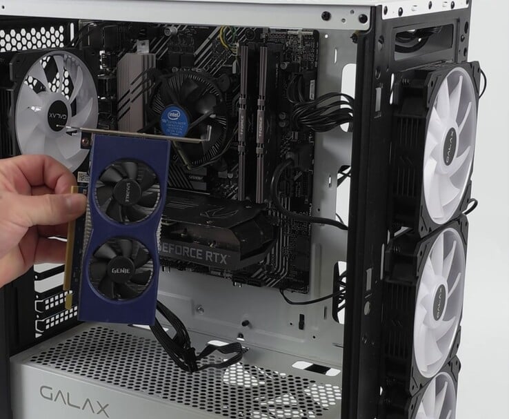 Uma mão segurando uma placa de vídeo Intel Arc A380 ao lado de um PC com uma Nvidia GeForce RTX 3060, preparada para uma configuração de GPU dupla com Lossless Scaling (Fonte da imagem: ETA PRIME via YouTube)
