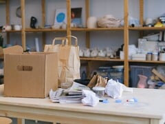 Caixa de papelão e sacolas de papel sobre uma mesa de madeira em um escritório com prateleiras
