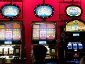 Máquinas caça-níqueis dentro de um cassino com telas iluminadas e pessoas jogando na frente (Fonte da imagem: djedj via Pixabay)