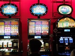 Máquinas caça-níqueis dentro de um cassino com telas iluminadas e pessoas jogando na frente (Fonte da imagem: djedj via Pixabay)