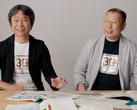 Uma captura de tela de Shigru Miyamoto e Tezuka Takashi usando camisetas do 30º aniversário de Super Mario Bros