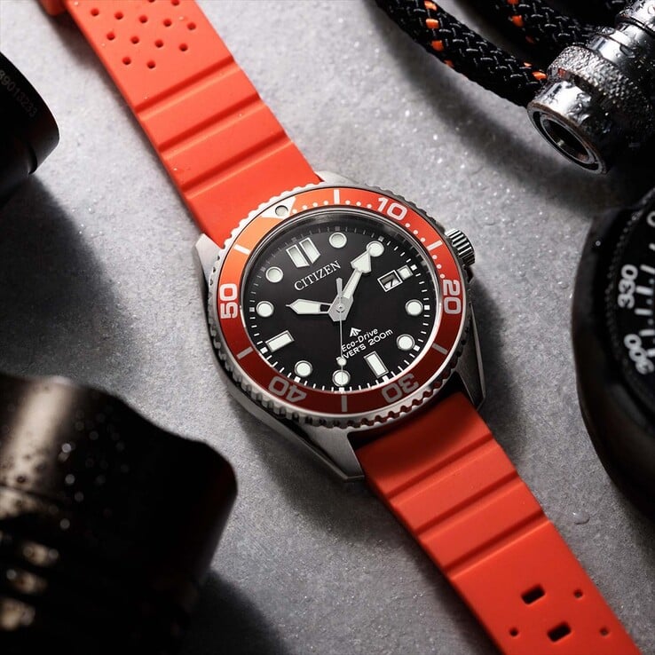 Relógio de mergulho Citizen Promaster Marine BN0268-01E com mostrador preto, luneta laranja e pulseira laranja, fotografado sobre uma superfície texturizada.