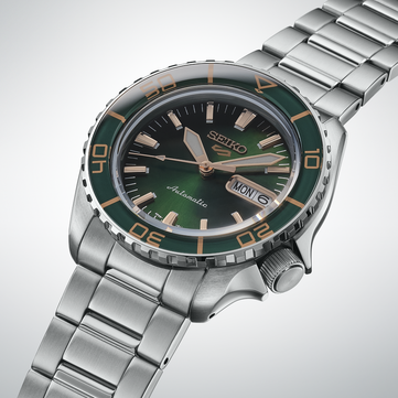 Close-up do Seiko 5 Sports SKX HDB005, destacando seu mostrador verde-escuro, ponteiros e índices aplicados na cor ouro rosa e luneta verde combinando com marcações douradas.