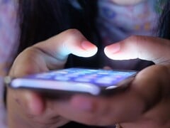 Duas mãos seguram um smartphone com a tela iluminada na penumbra
